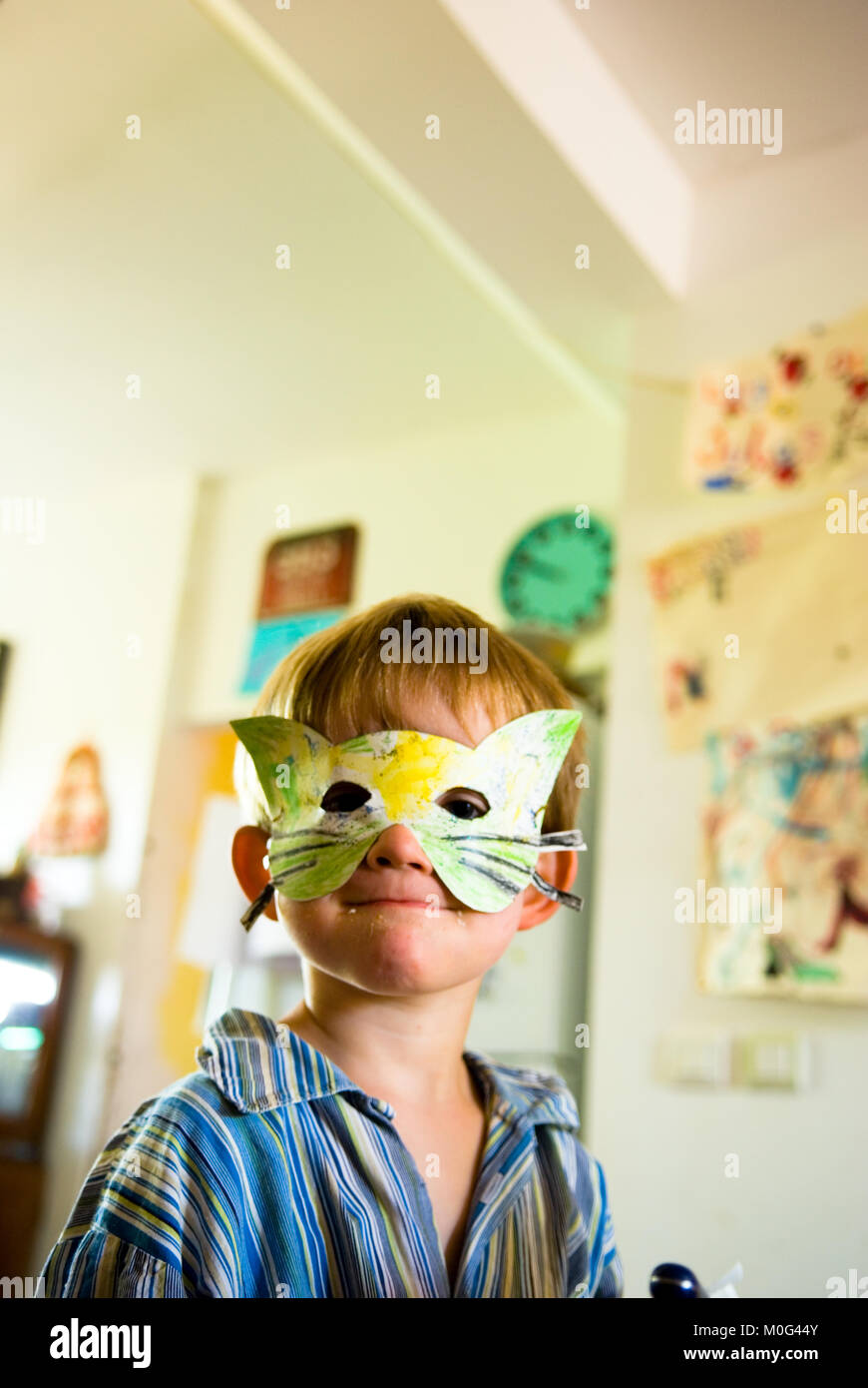 Un gros plan d'une année trois souriant dans son pyjama garçon portant un masque de chat à la main dans une cuisine domestique avec décorations et d'un réveil dans l'arrière-plan Banque D'Images