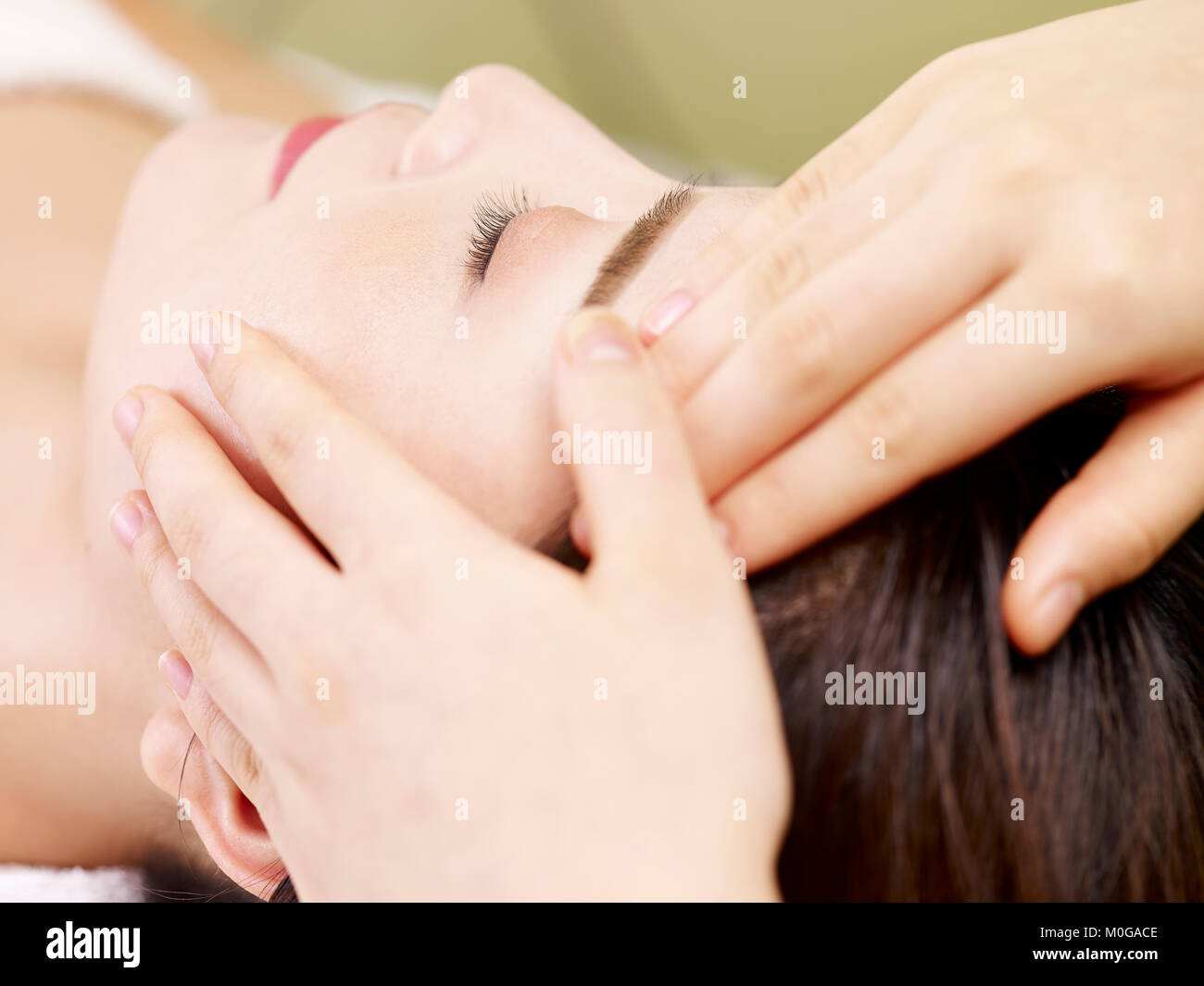 Close-up of beautiful young asian woman receiving massage du visage au spa de beauté, les yeux fermés. Banque D'Images