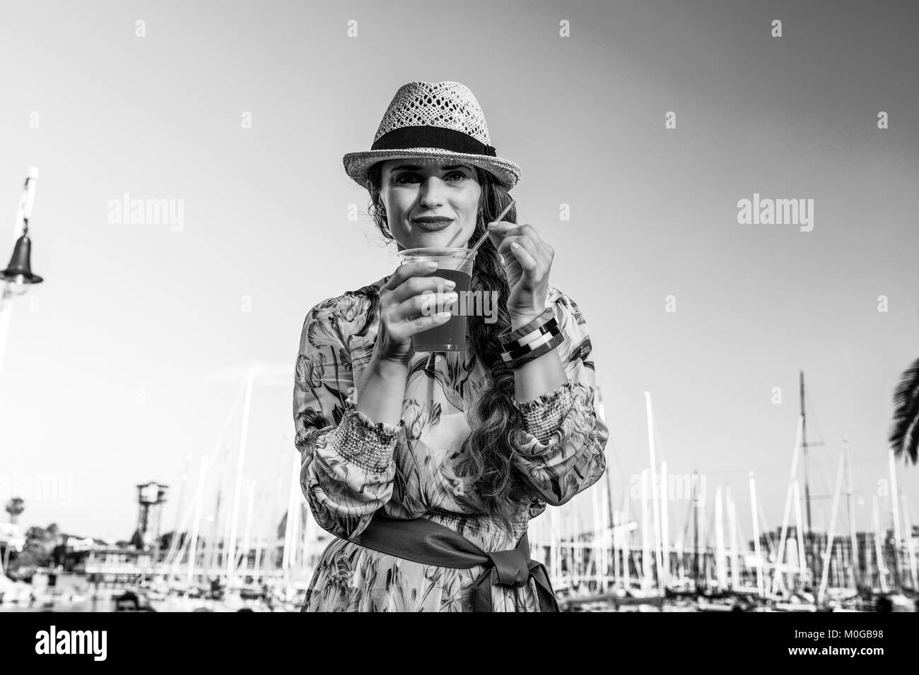 L'été à Barcelone. coloré femme touristique moderne en robe et chapeau de paille sur le quai à Barcelone, Espagne boire boissons rouge vif Banque D'Images