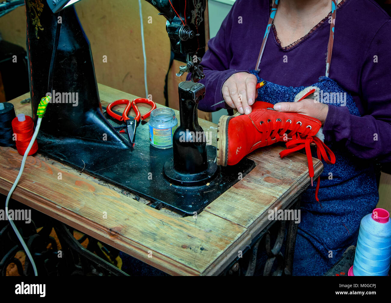 Un cordonnier de main de femme coud les bottes rouges en château.On la  machine à coudre sont le fil et les ciseaux Photo Stock - Alamy