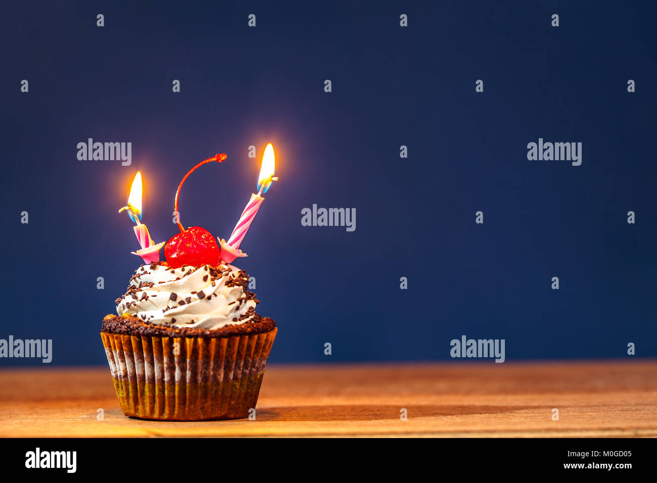 Birthday cupcake avec deux bougies allumées et une cerise rouge sur le  dessus sur fond bleu profond Photo Stock - Alamy
