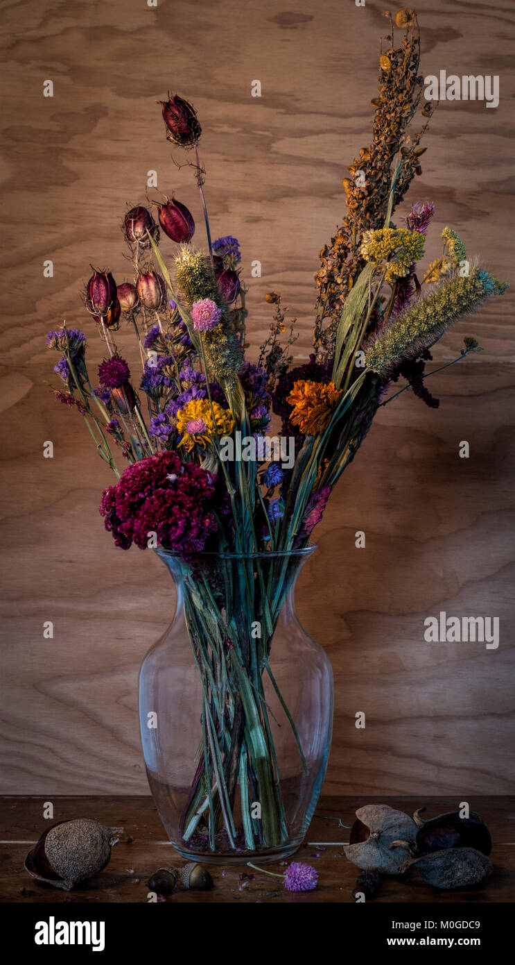 Nature morte de fleurs séchées dans un récipient en verre sur table en bois décoré avec des graines d'acorn et buckeye contre mur en bois Banque D'Images