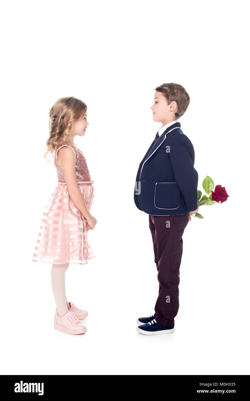 Vue latérale du garçon élégant in suit holding rose fleur et à la belle petite fille en robe rose en isolated on white Banque D'Images