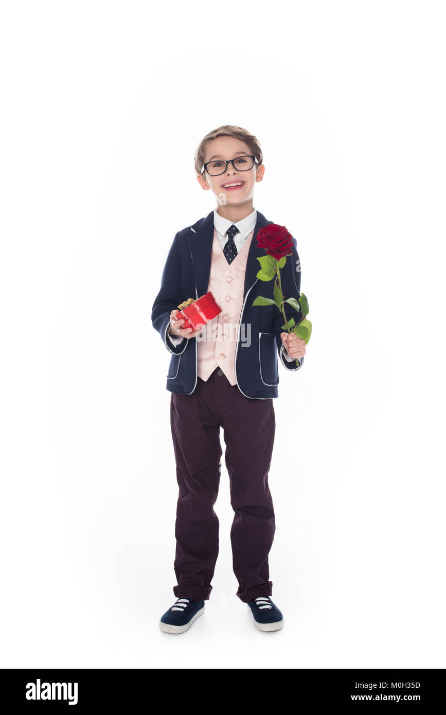 Cute little boy in suit holding et des lunettes en forme de coeur et fleurs rose red gift box isolated on white Banque D'Images