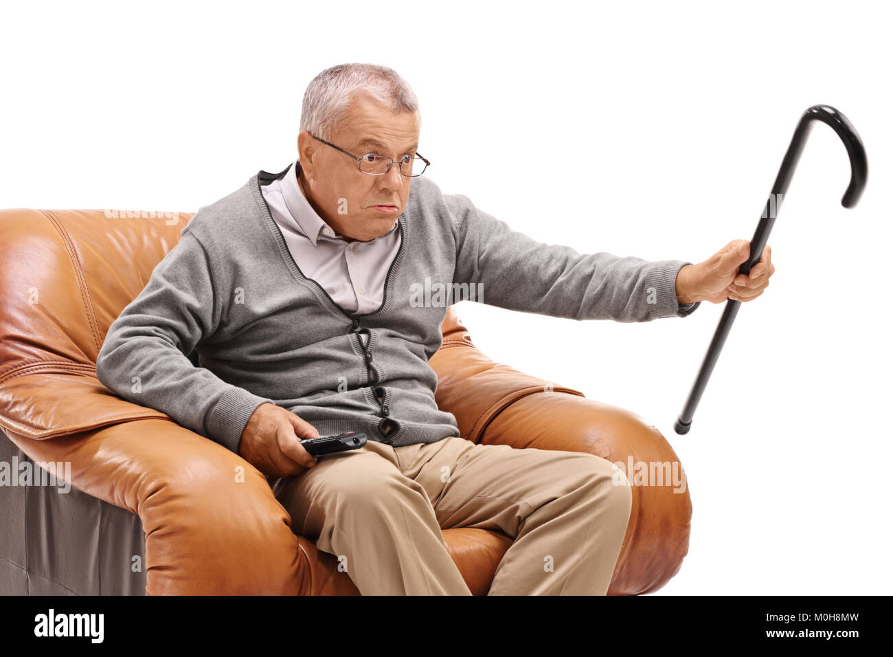 Avec une canne senior ennuyé assis dans un fauteuil et regarder la télévision isolé sur fond blanc Banque D'Images