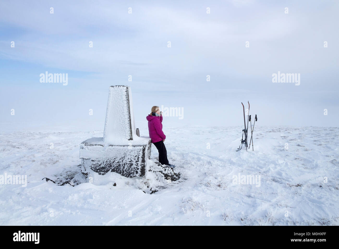 Tourer de ski en faisant une pause au sommet du siège Burnhope Trig en hiver, Cumbria/County Durham Royaume-uni Frontière Banque D'Images