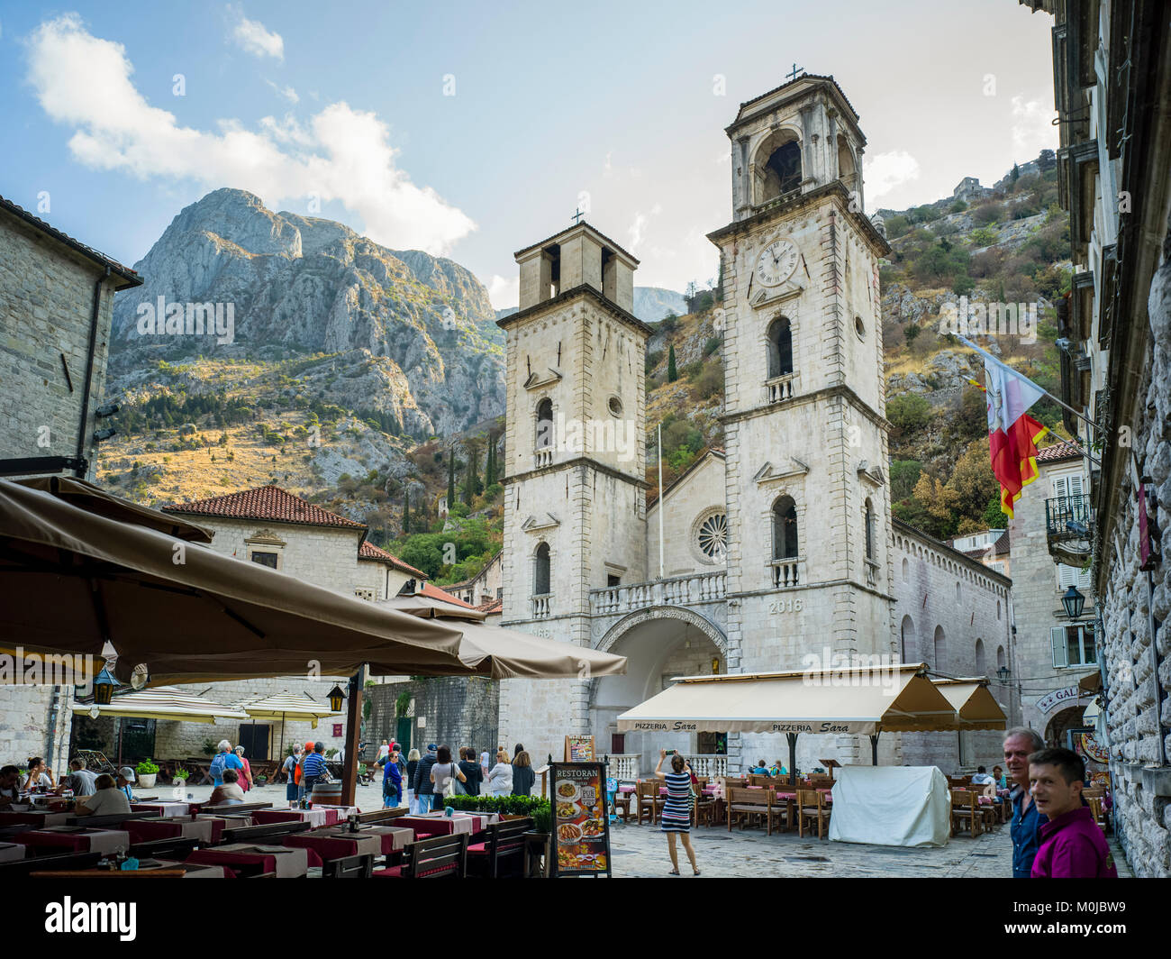 Les touristes dans les rues de Kotor avec restaurant en plein air d'un patio et d'un bâtiment d'église avec deux tours, Kotor, Kotor, Monténégro Municipalité Banque D'Images