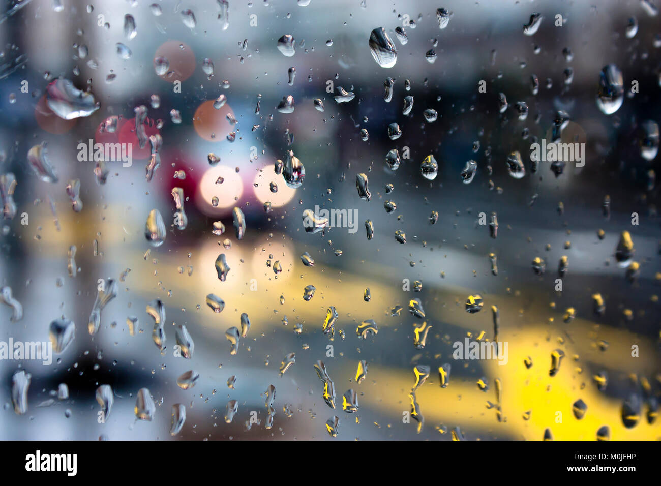 Résumé flou jour pluvieux, rue de ville à travers la fenêtre en verre avec des gouttes de pluie Banque D'Images
