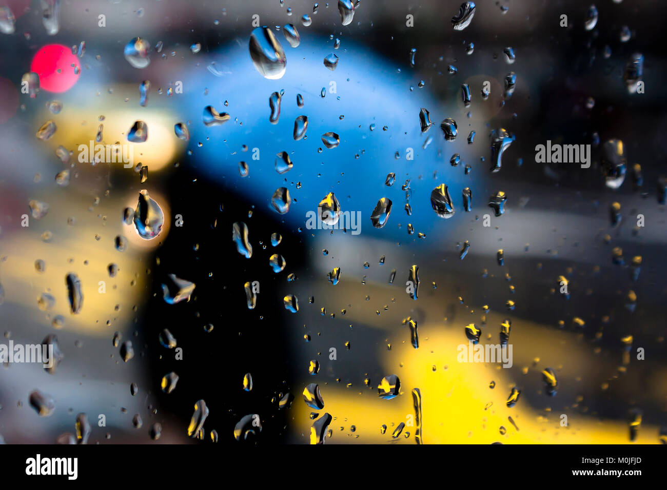 Résumé flou jour de pluie, la rue piétonne de la ville avec quelques sous par la fenêtre en verre avec parapluie gouttes Banque D'Images