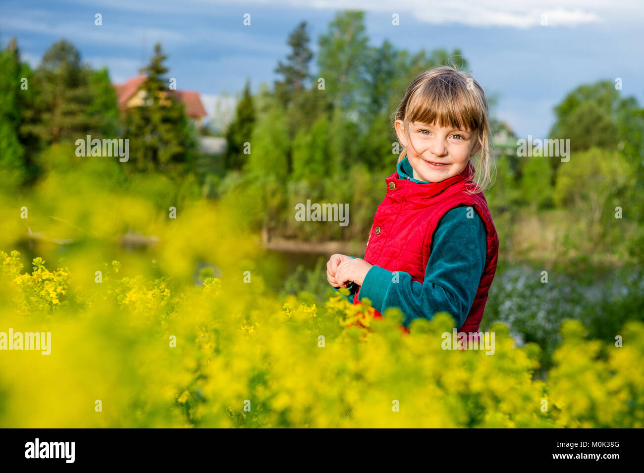 Petite fille qui marche à l'extérieur l'été prairie avec des fleurs jaunes (Barbarea vulgaris, Cresson d'hiver, hiver commune-cresson, roquette, jaune Banque D'Images