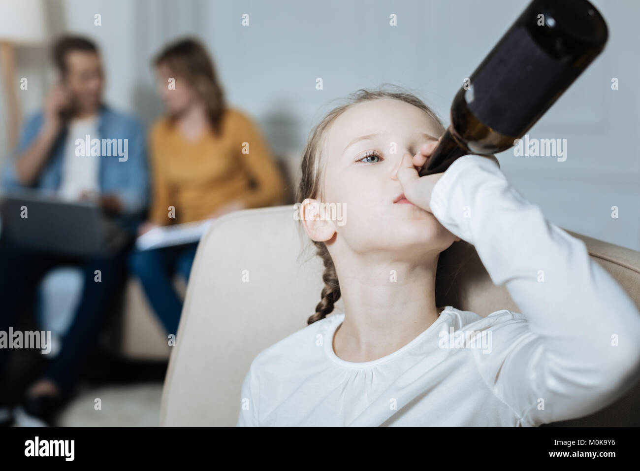 Misérable girl drinking pendant que les parents travaillent Banque D'Images