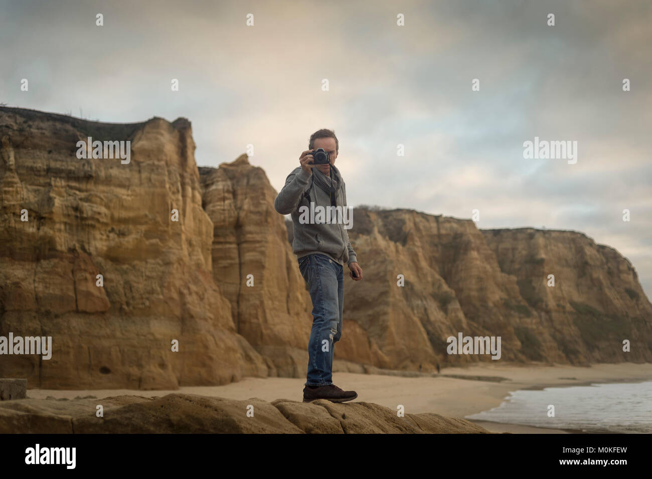 Homme debout sur les rochers par un littoral accidenté de prendre une photo. Banque D'Images Homme debout sur les rochers par un littoral accidenté de prendre une photo. Banque D'Images