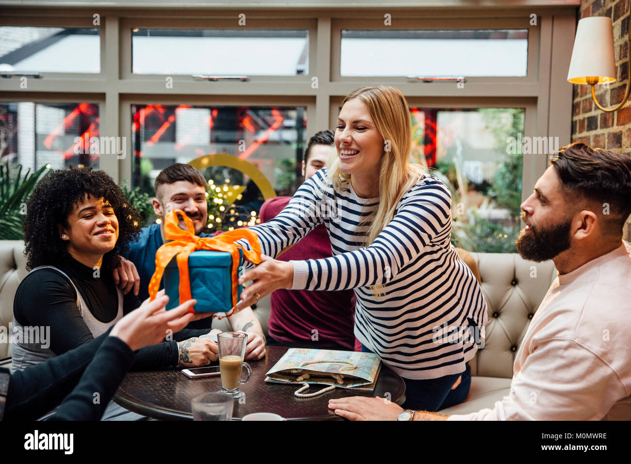 Les amis sont de traîner dans un bar, la célébration de l'un de l'anniversaire de la femme. Il est penché au-dessus de la table pour recevoir un cadeau. Banque D'Images