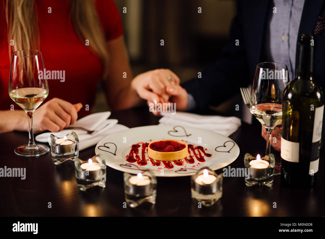 Couple sont dans un restaurant le jour de la Saint-Valentin. Ils ont un cœur framboise en forme de dessert et ont des bougies et du champagne sur la table. Banque D'Images