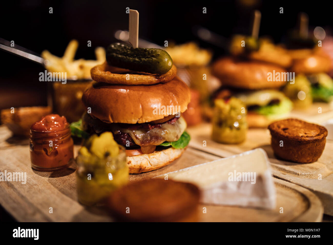 Gros plan d'un burger restaurant repas avec des oignons, du bacon, le cornichon, plaquettes et garnitures. Banque D'Images