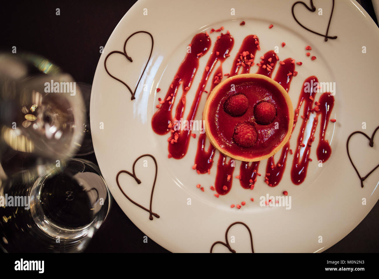 Passage tiré d'un dessert spécial Saint-Valentin dans un restaurant. Il s'agit d'une tarte aux framboises avec sauce au chocolat et coulis de cœurs. Banque D'Images