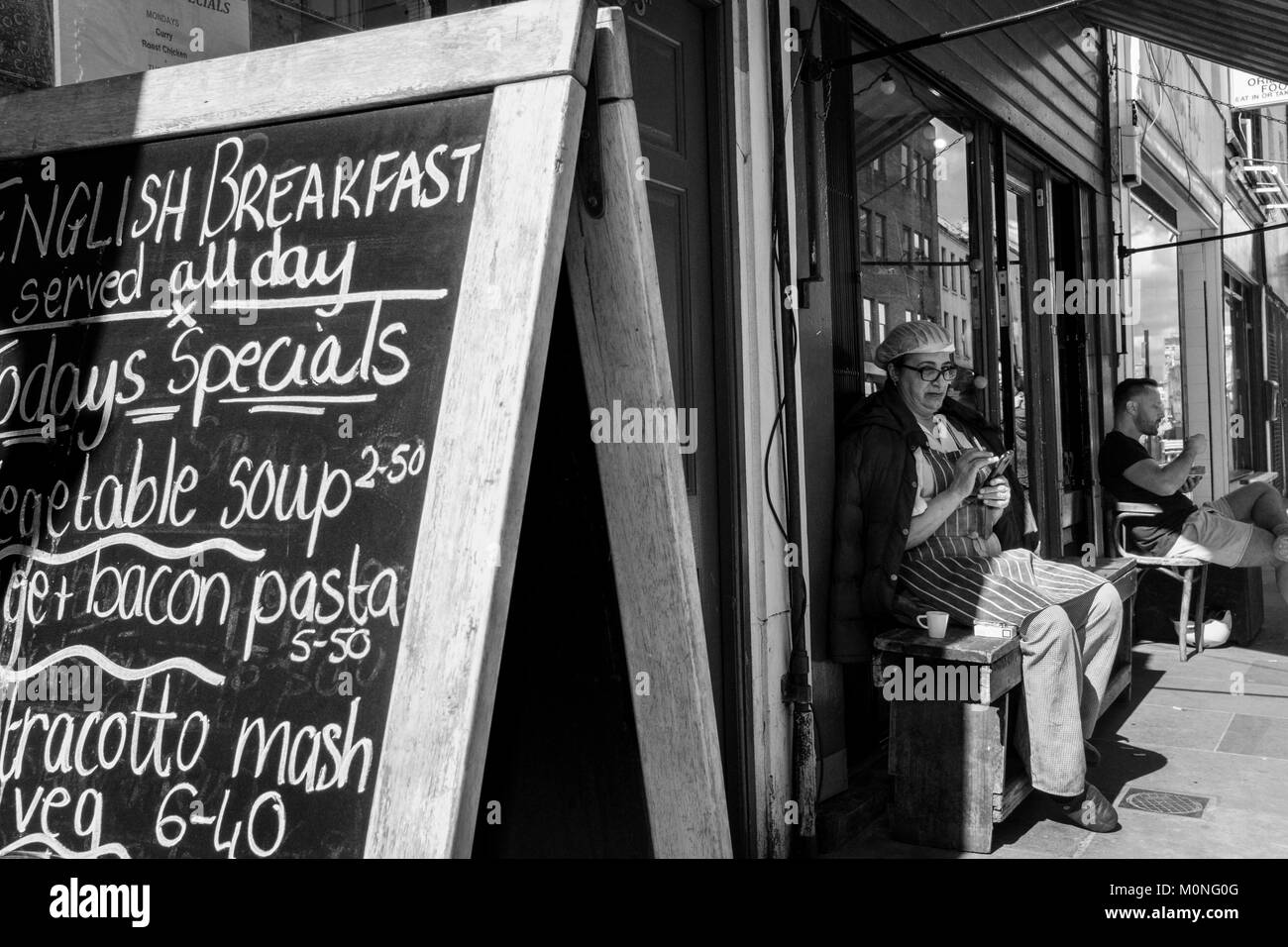 Photographie de rue en noir et blanc à Londres : une femme qui fait une pause au travail à l'extérieur d'un café, Lower Marsh, Londres. Banque D'Images