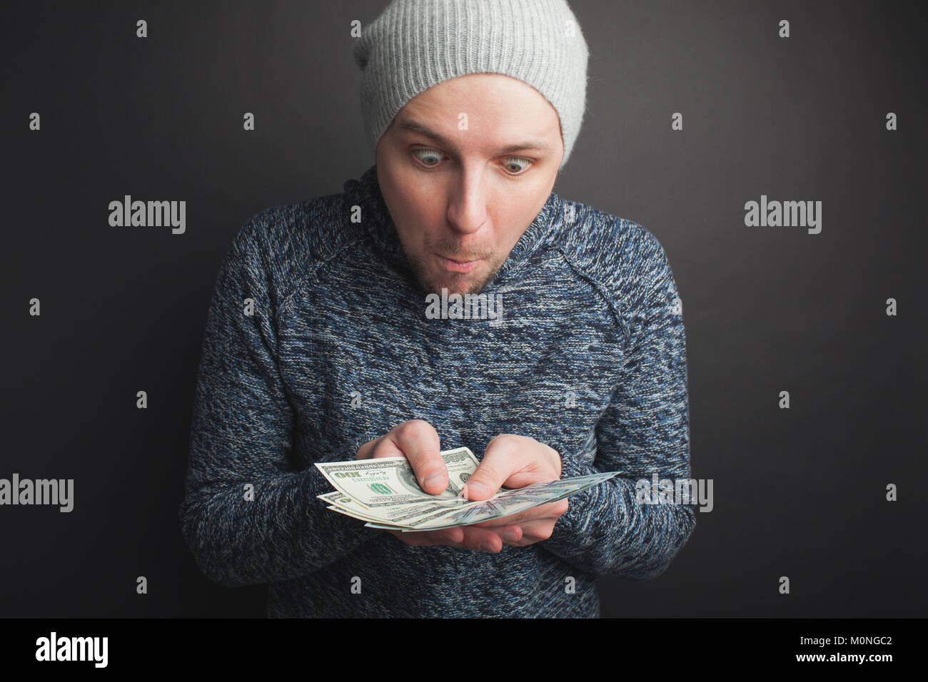 Un jeune mec dans un capuchon gris et une barbe, tenant une pile de l'argent et regarde-le sur un fond noir. Freelancer admirer ses ses gains dans l'Inte Banque D'Images