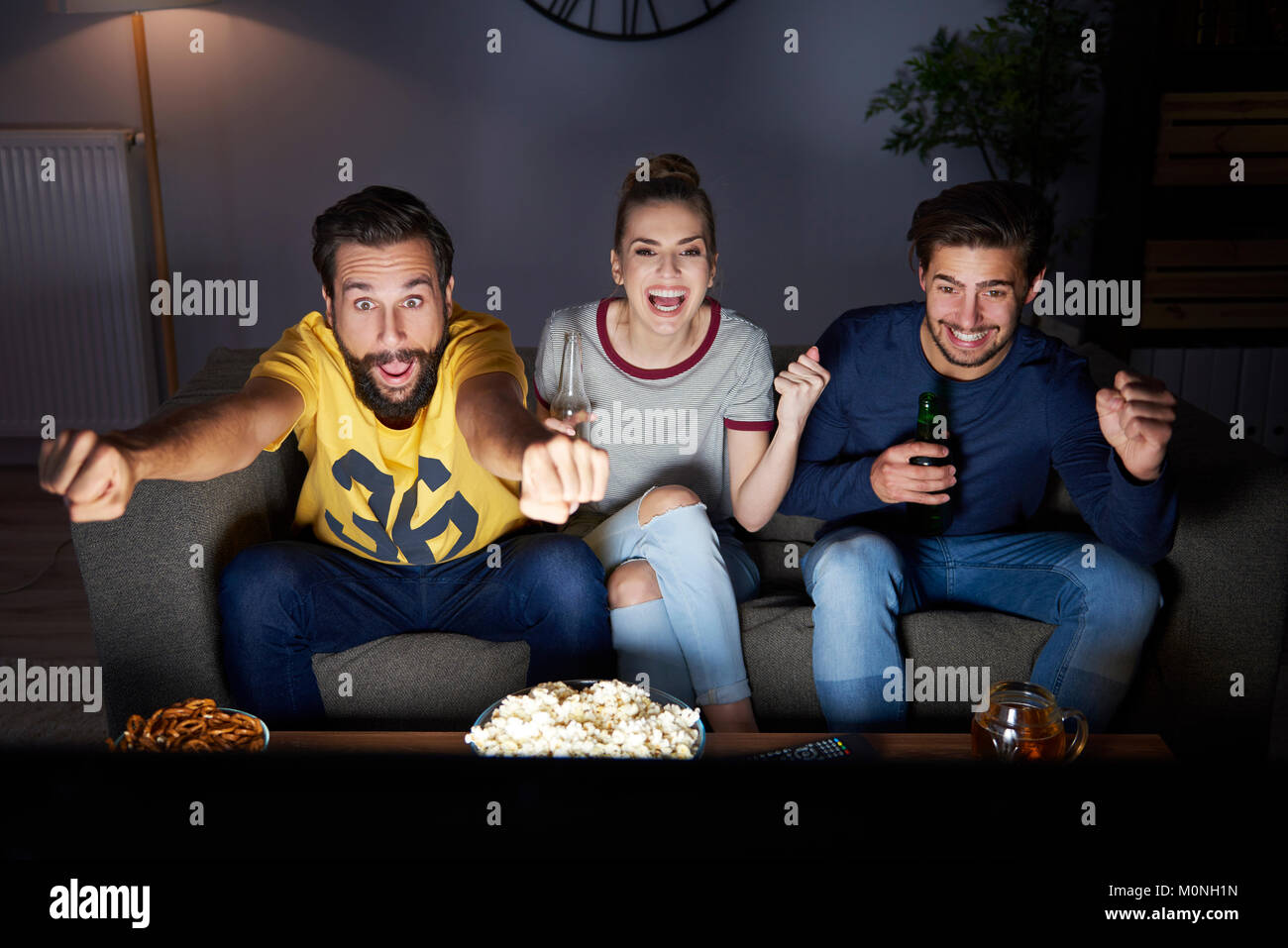 Heureux les amis assis sur le canapé en regardant la télé Banque D'Images