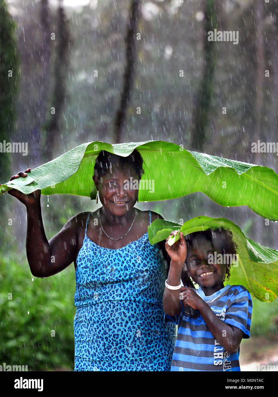 La mère et l'enfant à l'aide de feuilles de banane comme parapluie contre la pluie torrentielle. Jungle de l'île de Bougainville, en Papouasie-Nouvelle-Guinée. (Image) manipulées numériquement Banque D'Images
