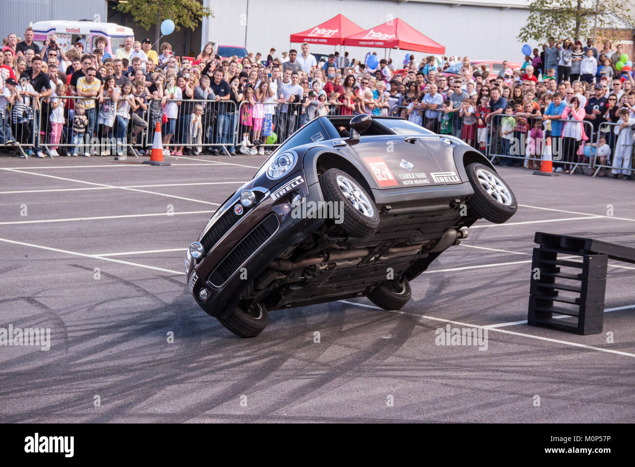 La foule regarder un stunt pilote dans une nouvelle BMW mini lecteur sur deux roues. Banque D'Images