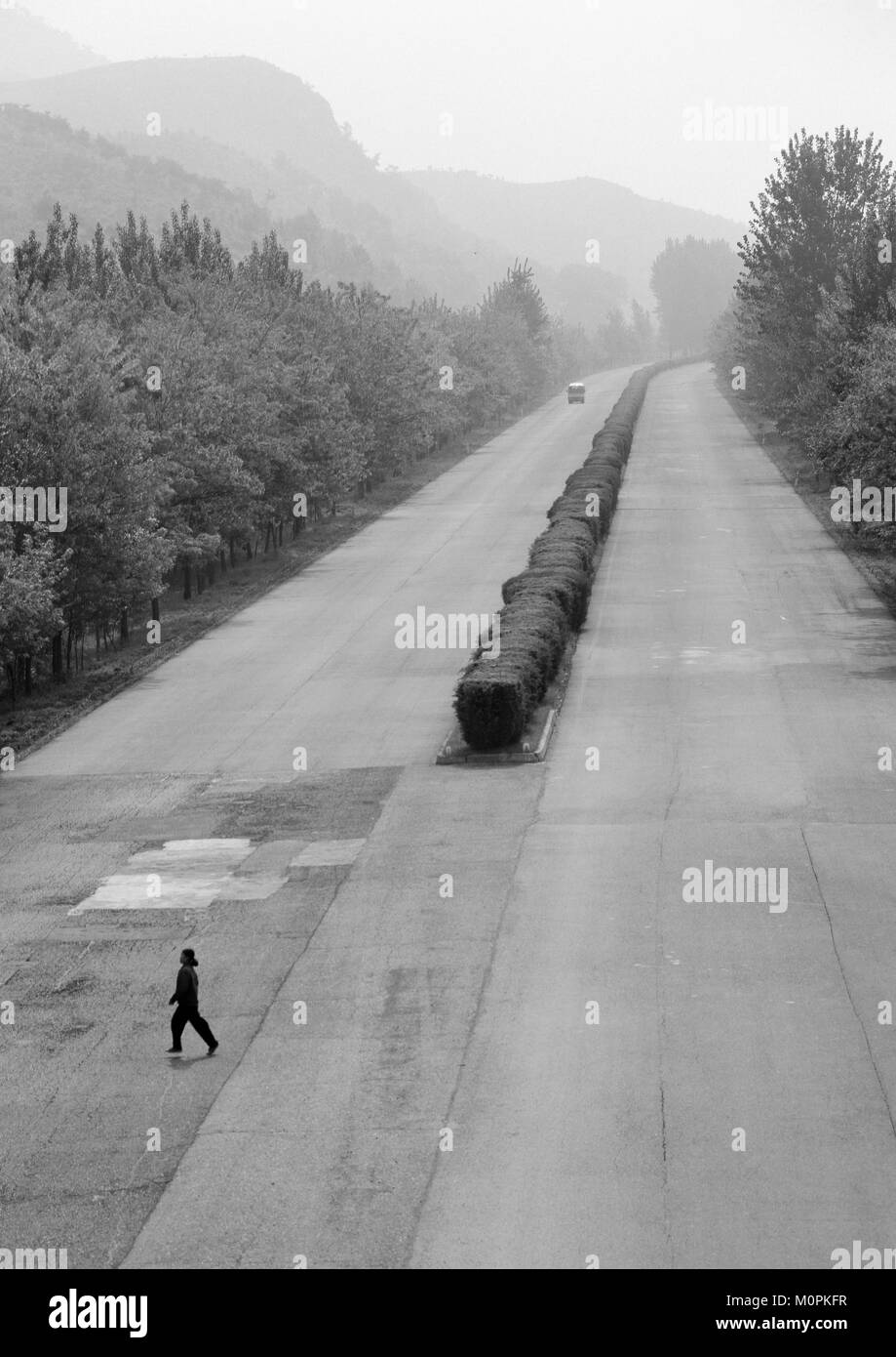 Femme Corée du Nord traversant l'autoroute vide avec un bus arrivant dans la distance, de la province de Pyongan, Pyongyang, Corée du Nord Banque D'Images