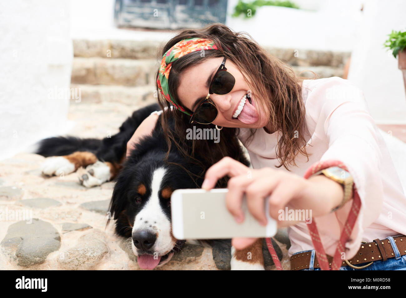 Fille brune en tenant des selfies un mignon bernois se trouvant sur le plancher fatigué et elle. Banque D'Images