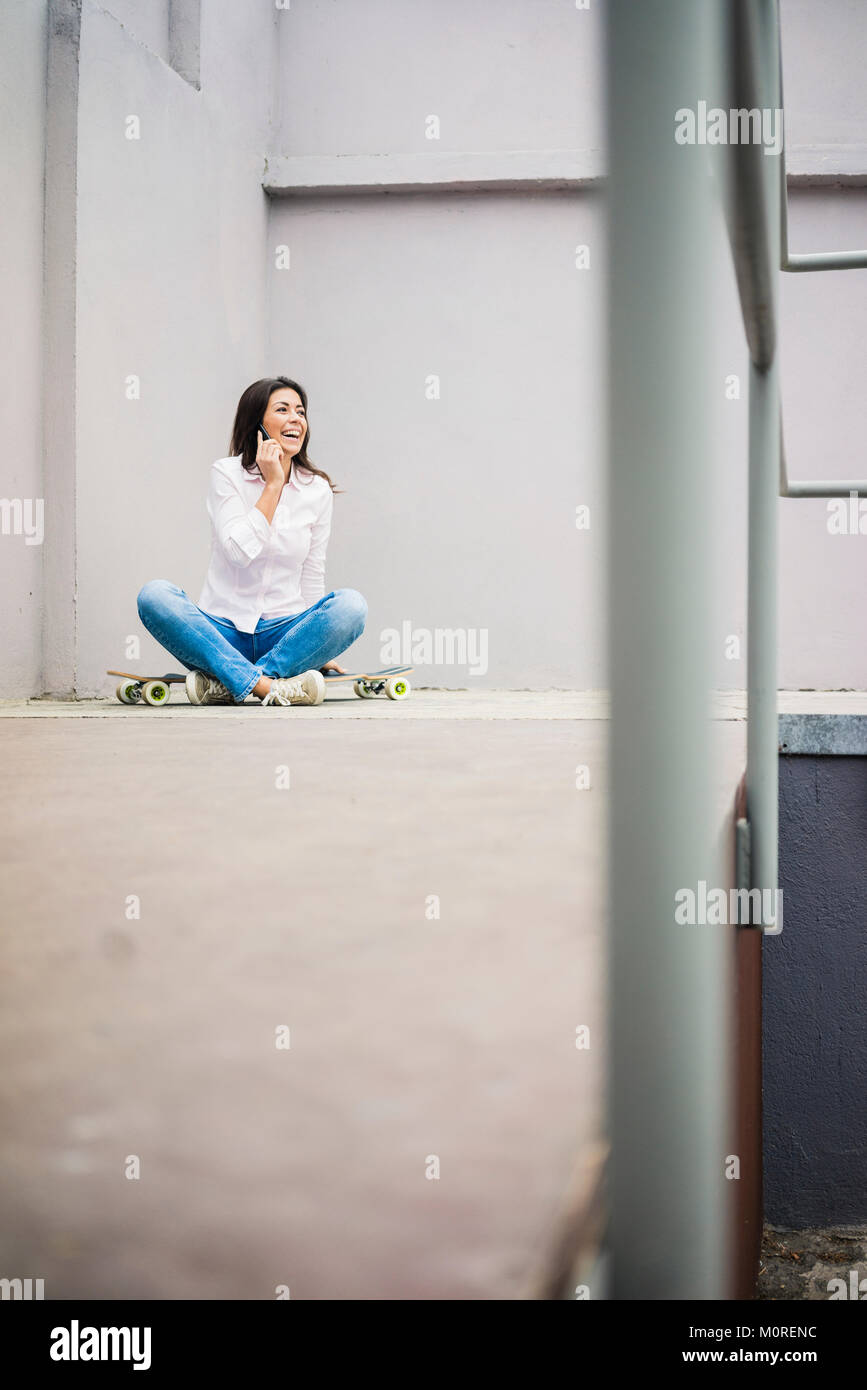Laughing young woman on the phone sitting on skateboard Banque D'Images