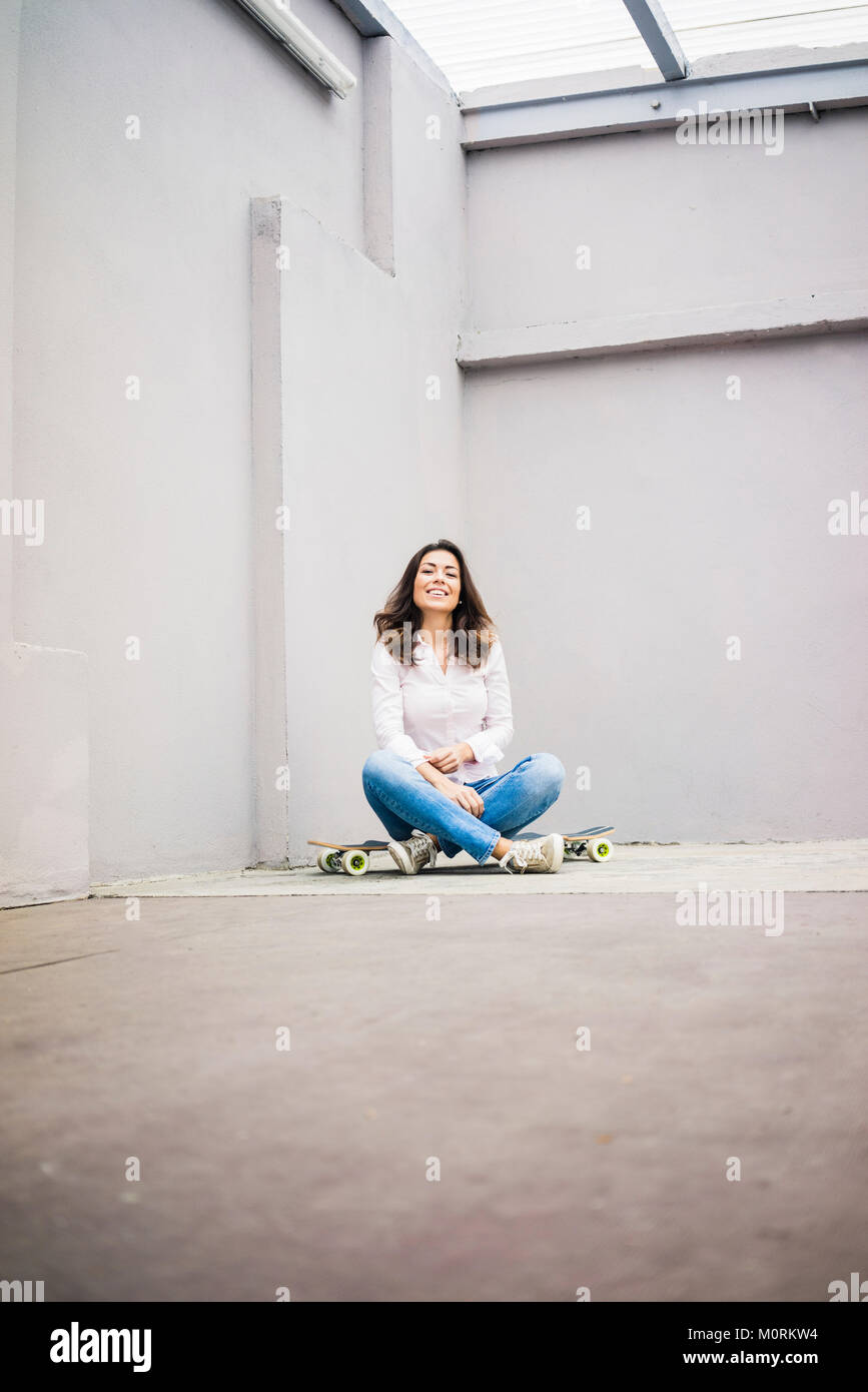 Smiling young woman sitting on skateboard sur terrasse Banque D'Images