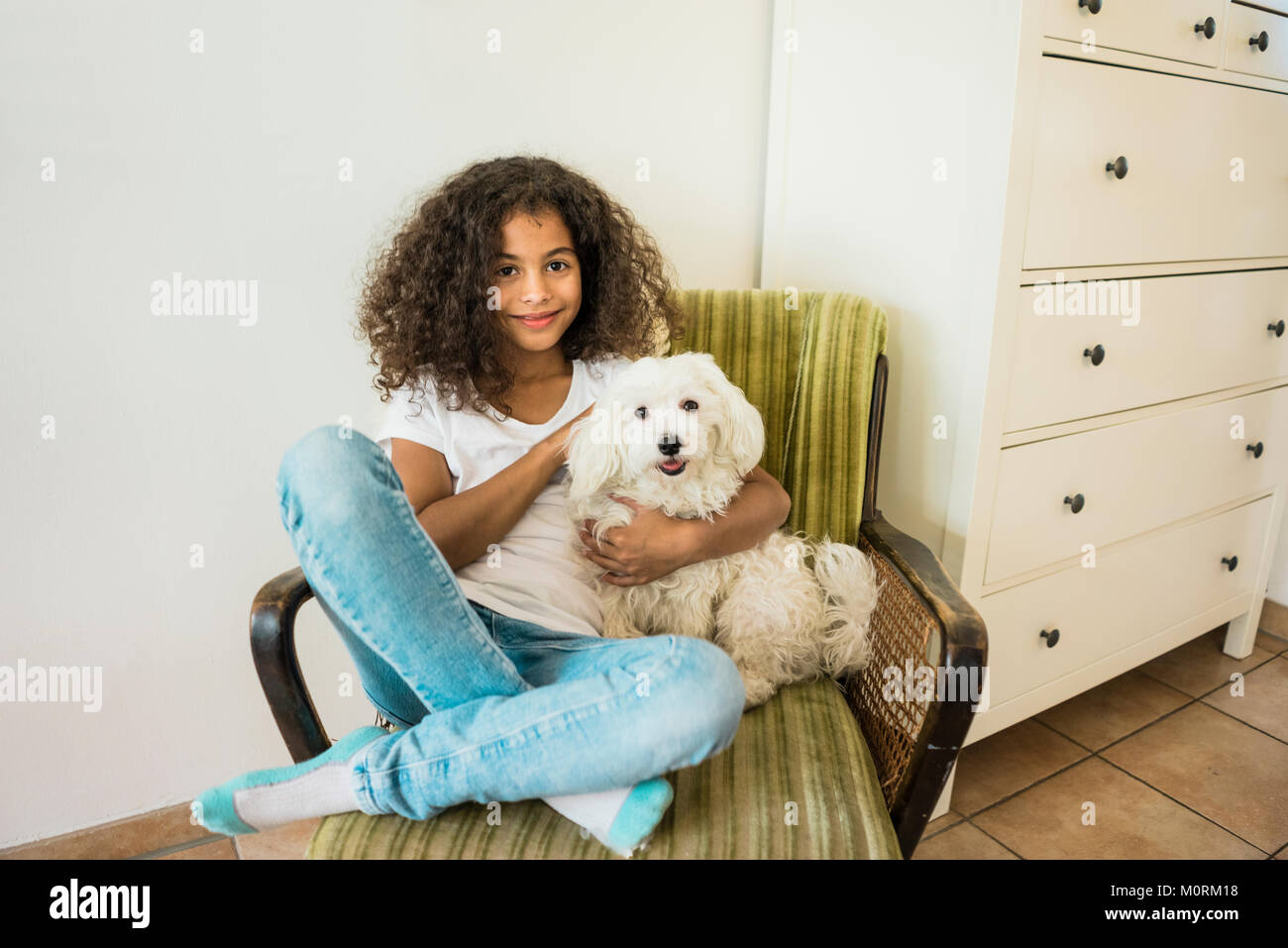 L'amour des animaux petite fille assise dans un fauteuil de flatter son chien blanc Banque D'Images