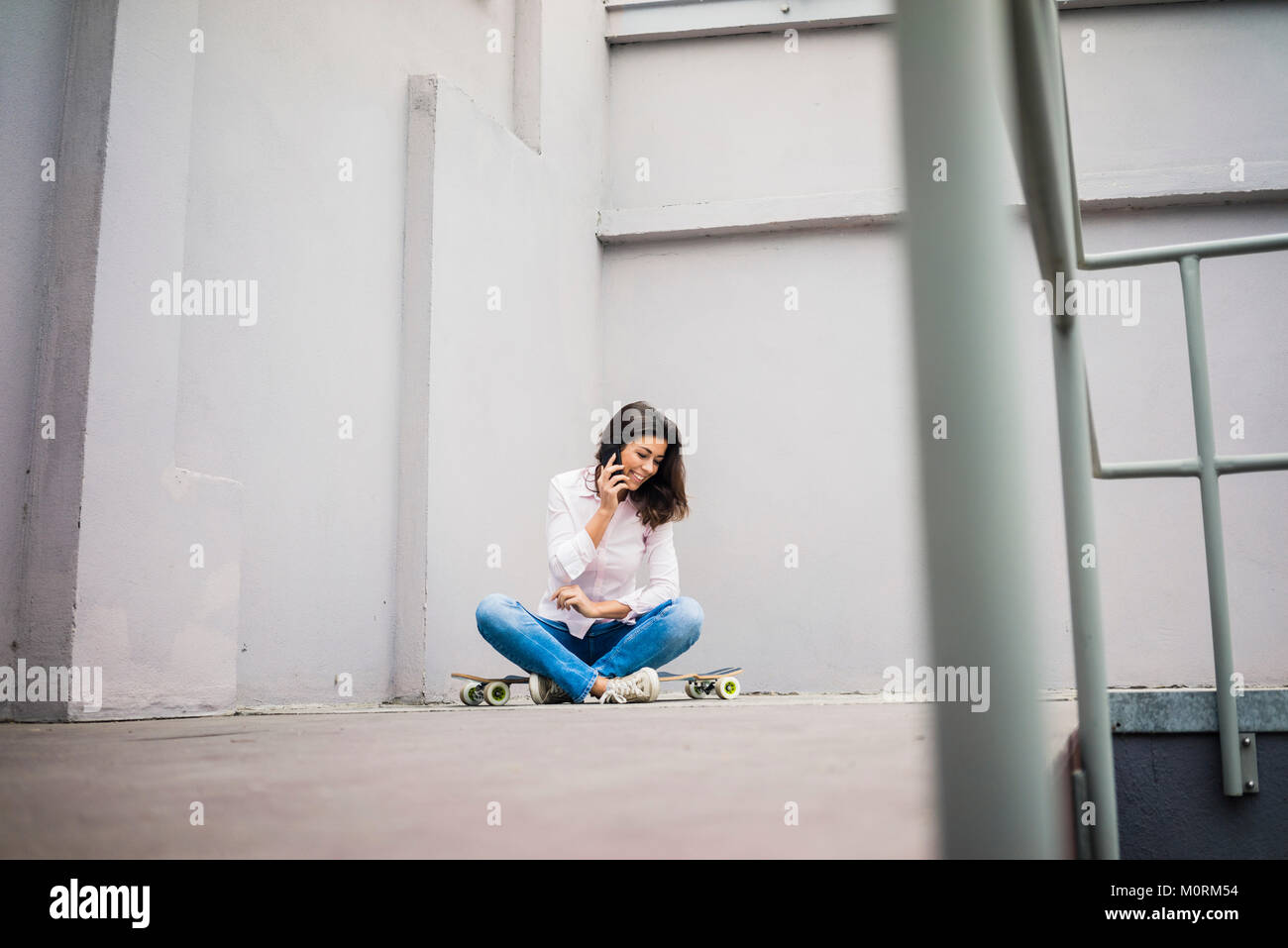 Smiling young woman on the phone sitting on skateboard Banque D'Images