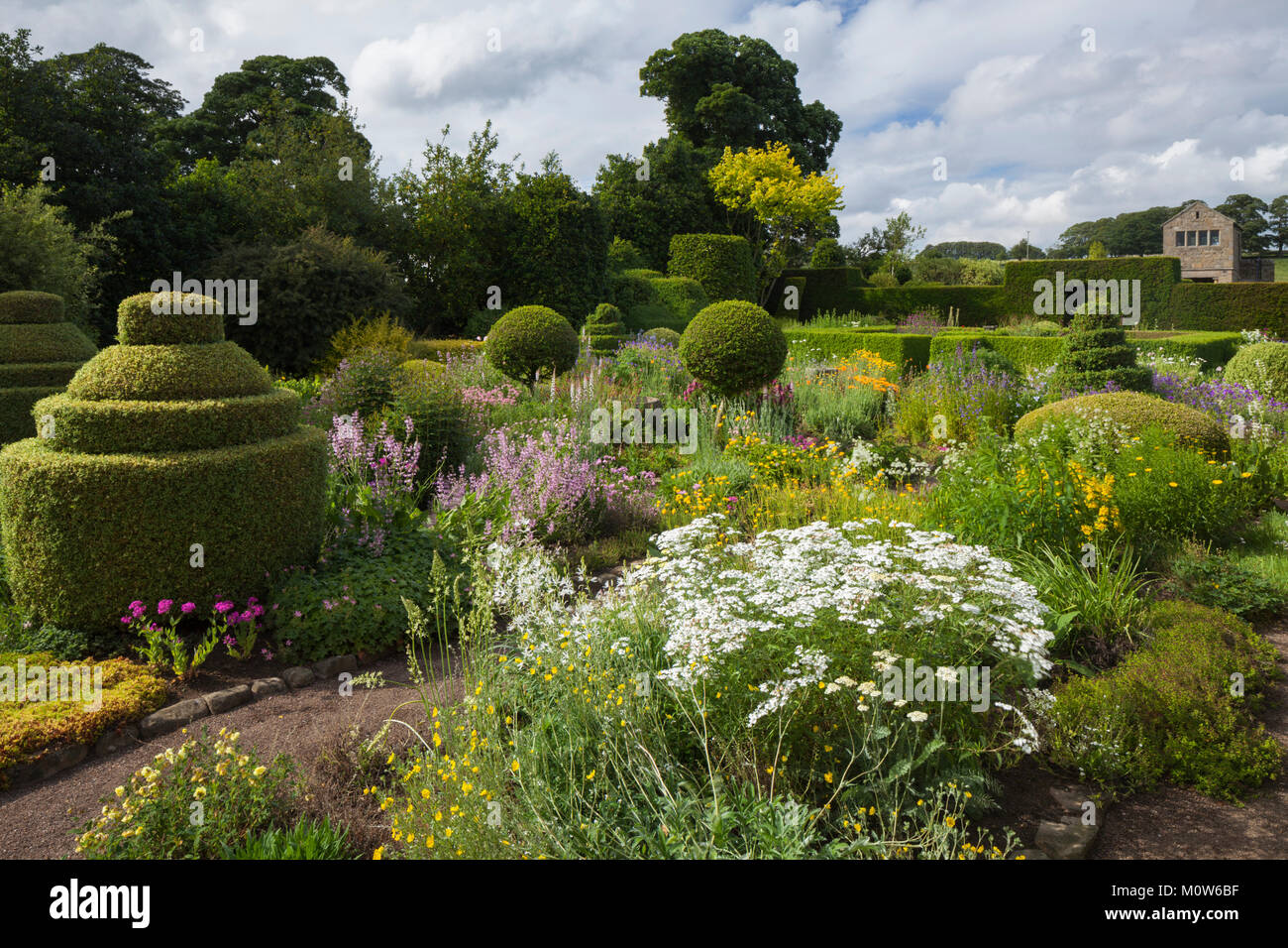 Colorés et topiaires plantes frontières de la fleur jardin avec un pavillon à l'arrière-plan, Herterton House gardens, Northumberland, England Banque D'Images