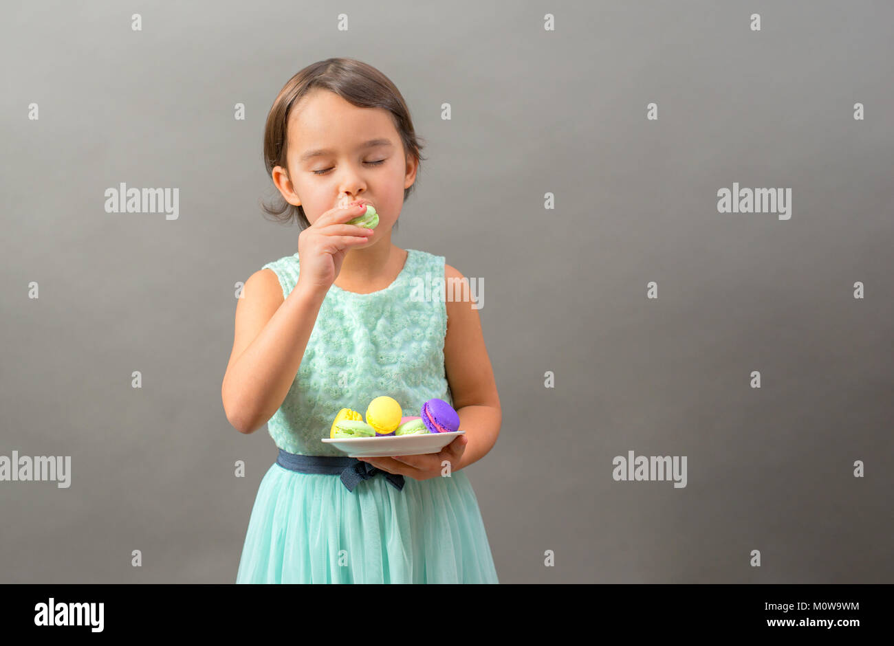 Petite fille excité avec une assiette pleine de macarons Banque D'Images