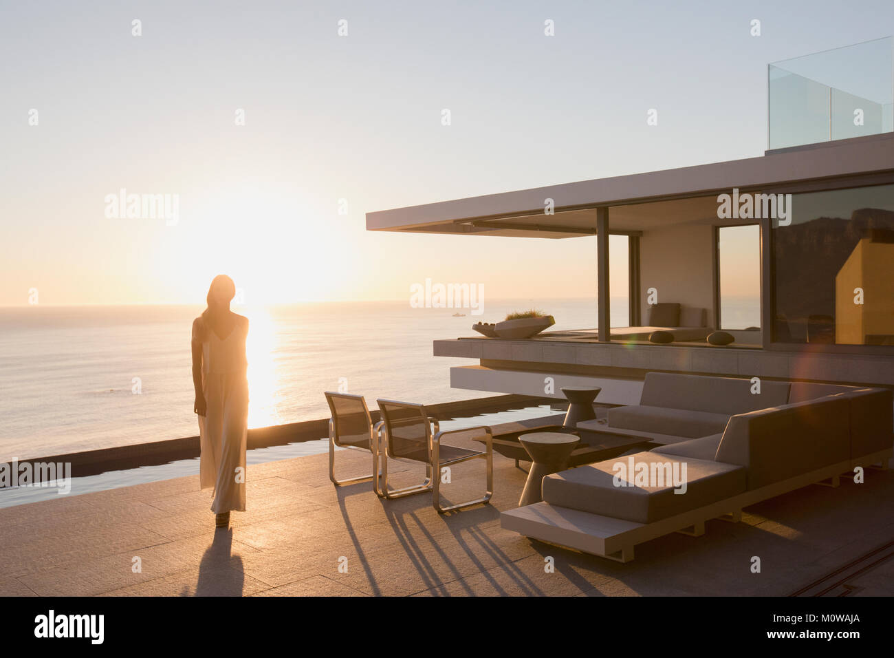 Femme marche sur modern, luxury home vitrine pont extérieur avec vue sur l'océan au coucher du soleil Banque D'Images
