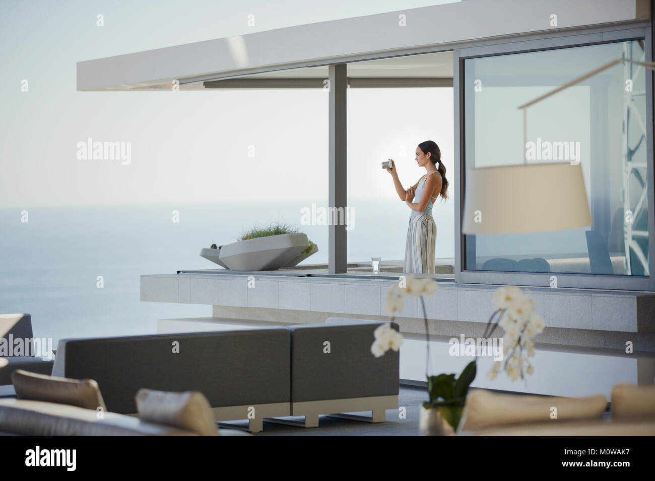 Femme avec appareil photo numérique la photographie moderne, vue sur l'océan sur luxury home showcase balcon Banque D'Images