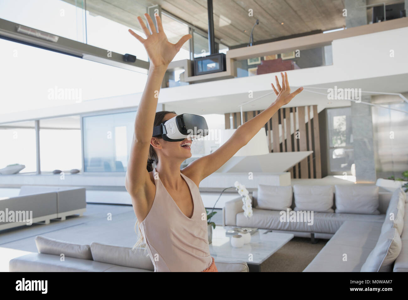 Femme énergique à l'aide du simulateur de réalité virtuelle avec bras levés en lunettes, luxe moderne home vitrine salon Banque D'Images
