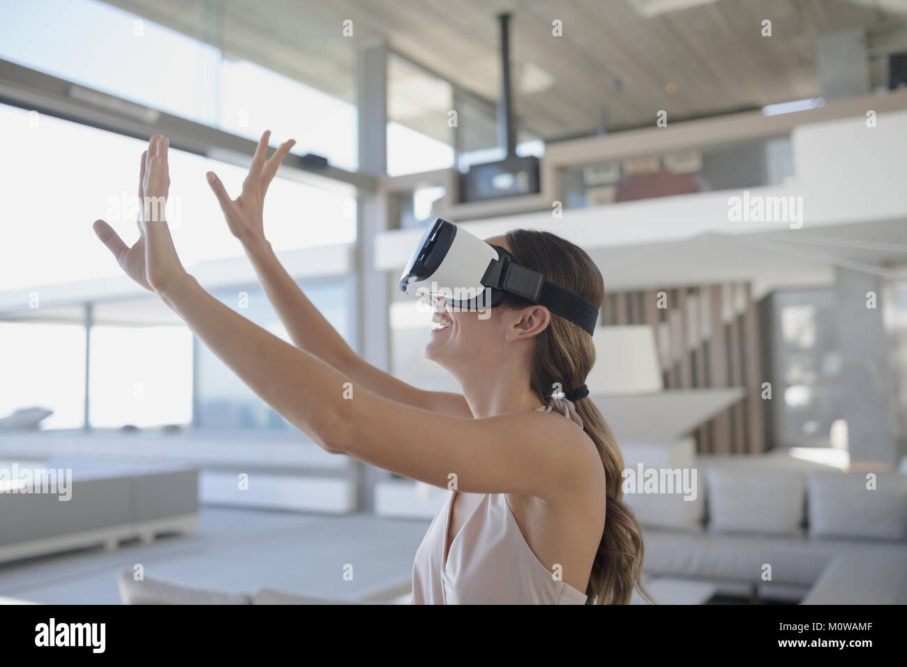 Smiling woman Using virtual reality simulator lunettes avec bras levés en maison de luxe moderne, salon showcase Banque D'Images