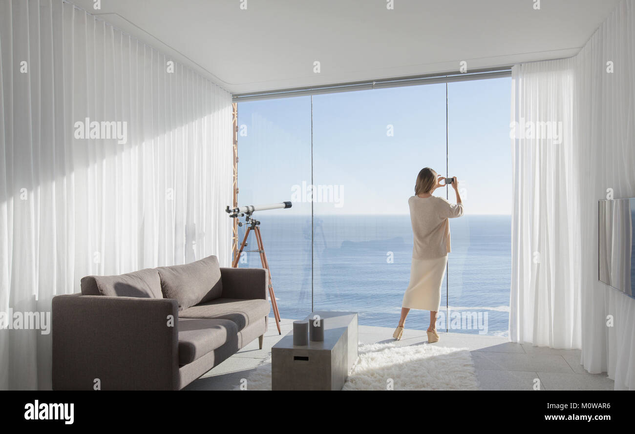 Femme avec téléphone appareil photo photographier sunny vue mer à partir de hôtel moderne et luxueux home vitrine salon intérieur Banque D'Images