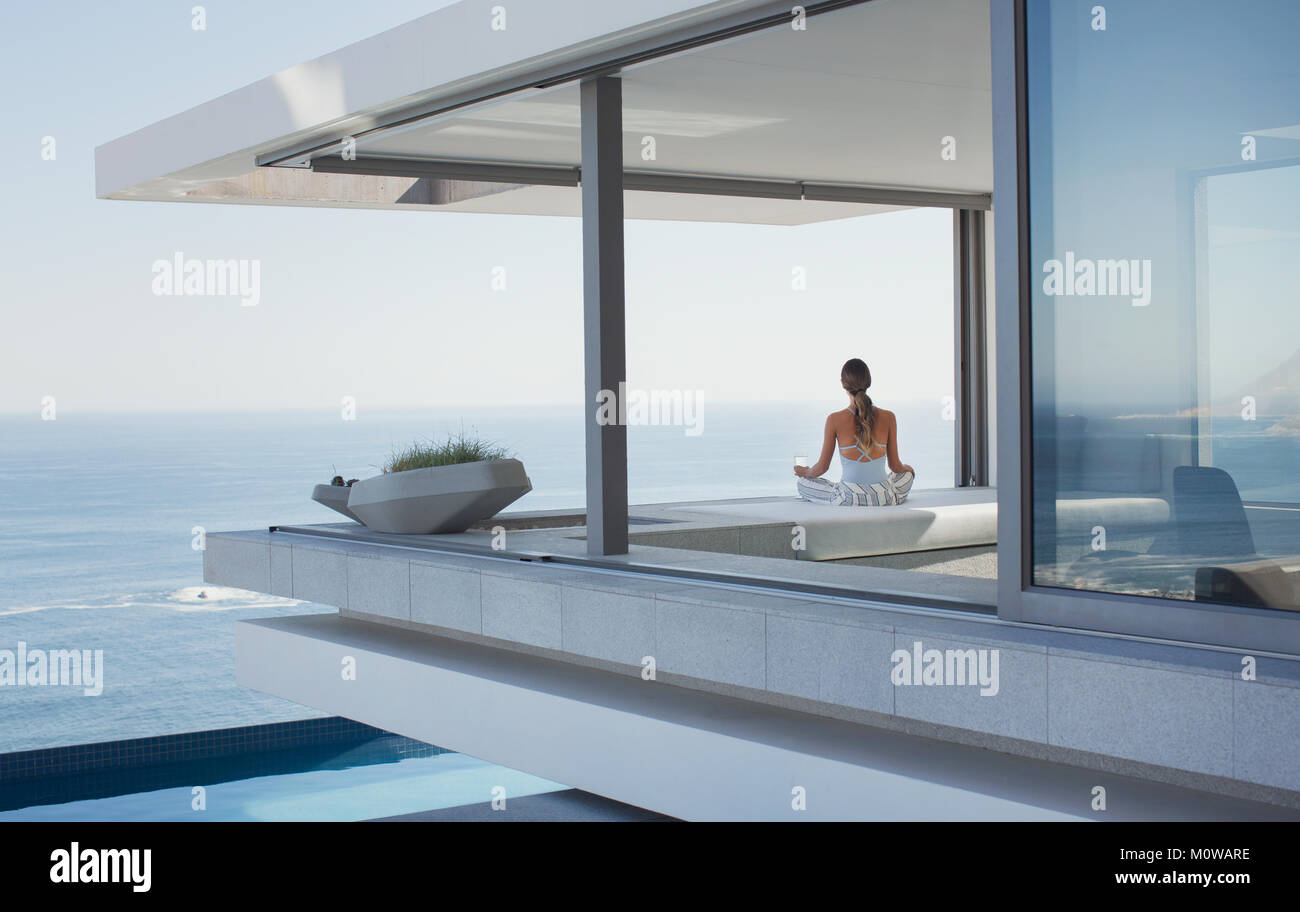 Serene woman meditating on modern, luxury home vitrine patio extérieur avec vue sur l'océan Banque D'Images