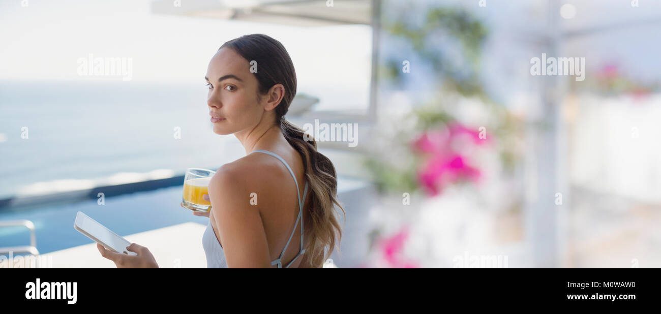 Brunette woman drinking orange juice and using digital tablet sur patio de luxe Banque D'Images