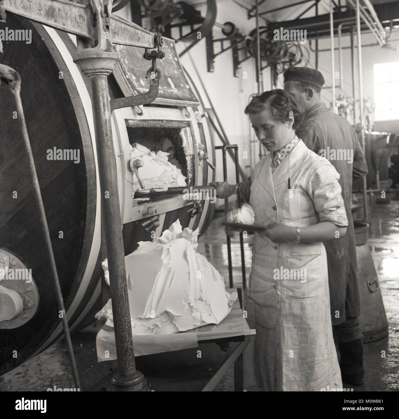 Années 1950, historique, un travailleur féminin vérifie le beurre produit à partir d'un tambour en bois cylindrique de grande taille d'une petite crémerie dans le sud de l'Irlande. Banque D'Images