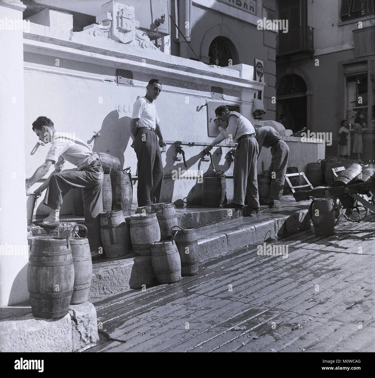 Années 1950, photo historique montrant l 'Auguadores" (vendeurs) de l'eau remplissant leurs fûts de bois avec de l'eau de la touche lors d'une citerne près de Governor's Parade, Gibraltar. Ces hommes utilisés pour fournir l'eau à des propriétés dans le centre, particulièrement les maisons plus anciennes, dont la majorité n'avait pas l'eau courante à cette époque. Banque D'Images