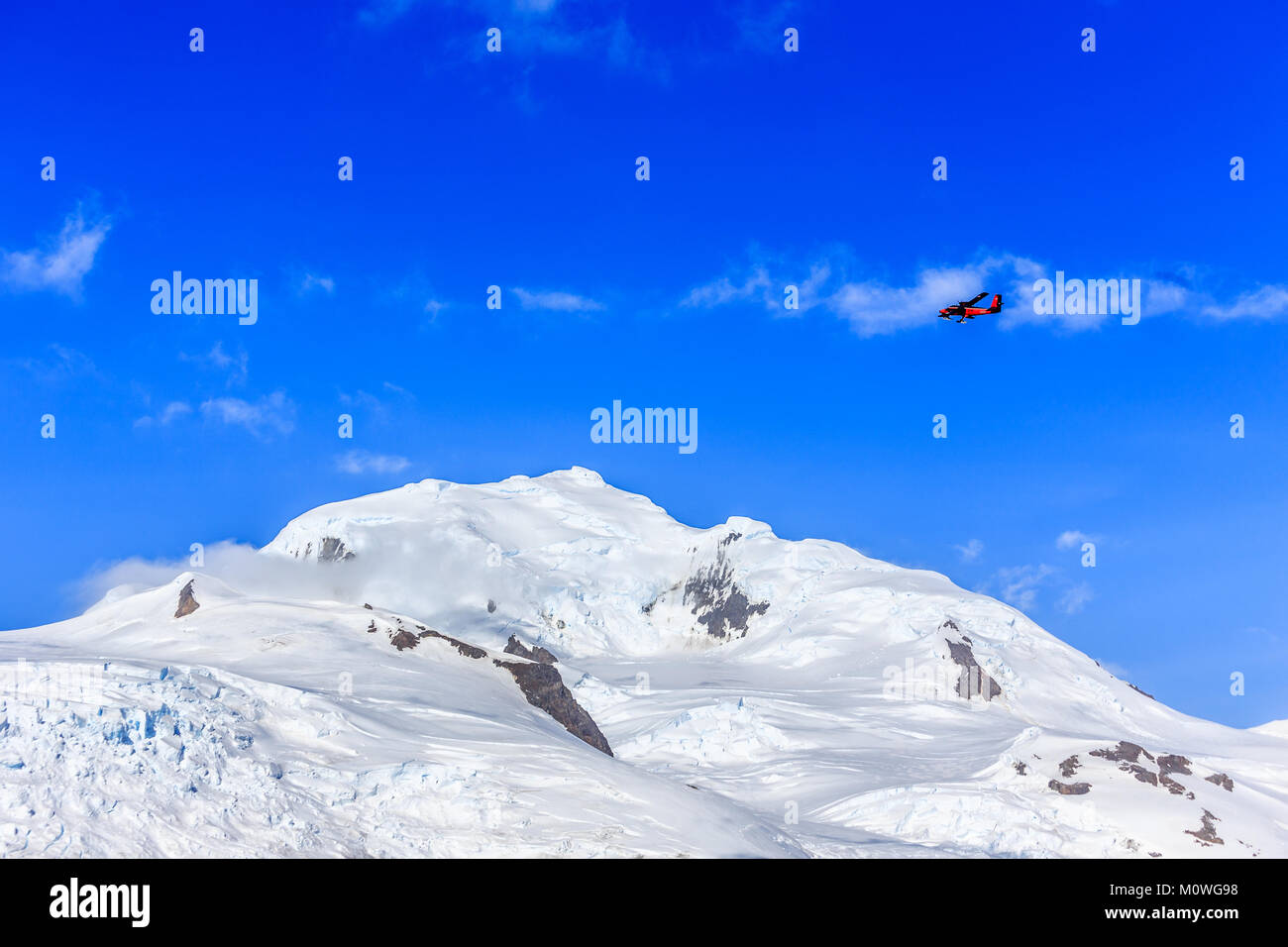 Petit avion rouge voler parmi les nuages au-dessus de pics de neige et glaciers, Hald Moon island, Antarctic peninsula Banque D'Images