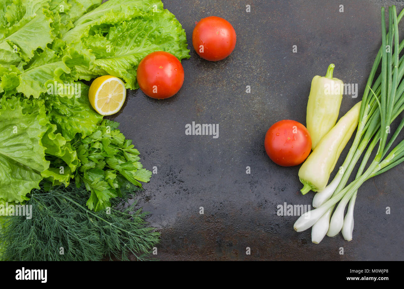 Laitue avec aneth, persil, citron, tomates et oignons rouges vert gros plan sur un fond de texture sombre Banque D'Images