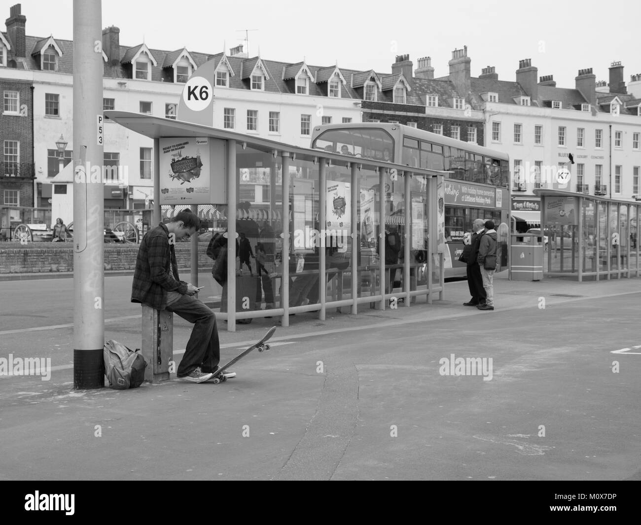 Jeune homme avec skateboard à l'arrêt de bus (monochrome) Banque D'Images
