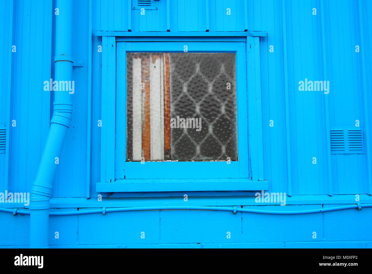 Petite fenêtre sur mur de métal ondulé bleu Banque D'Images