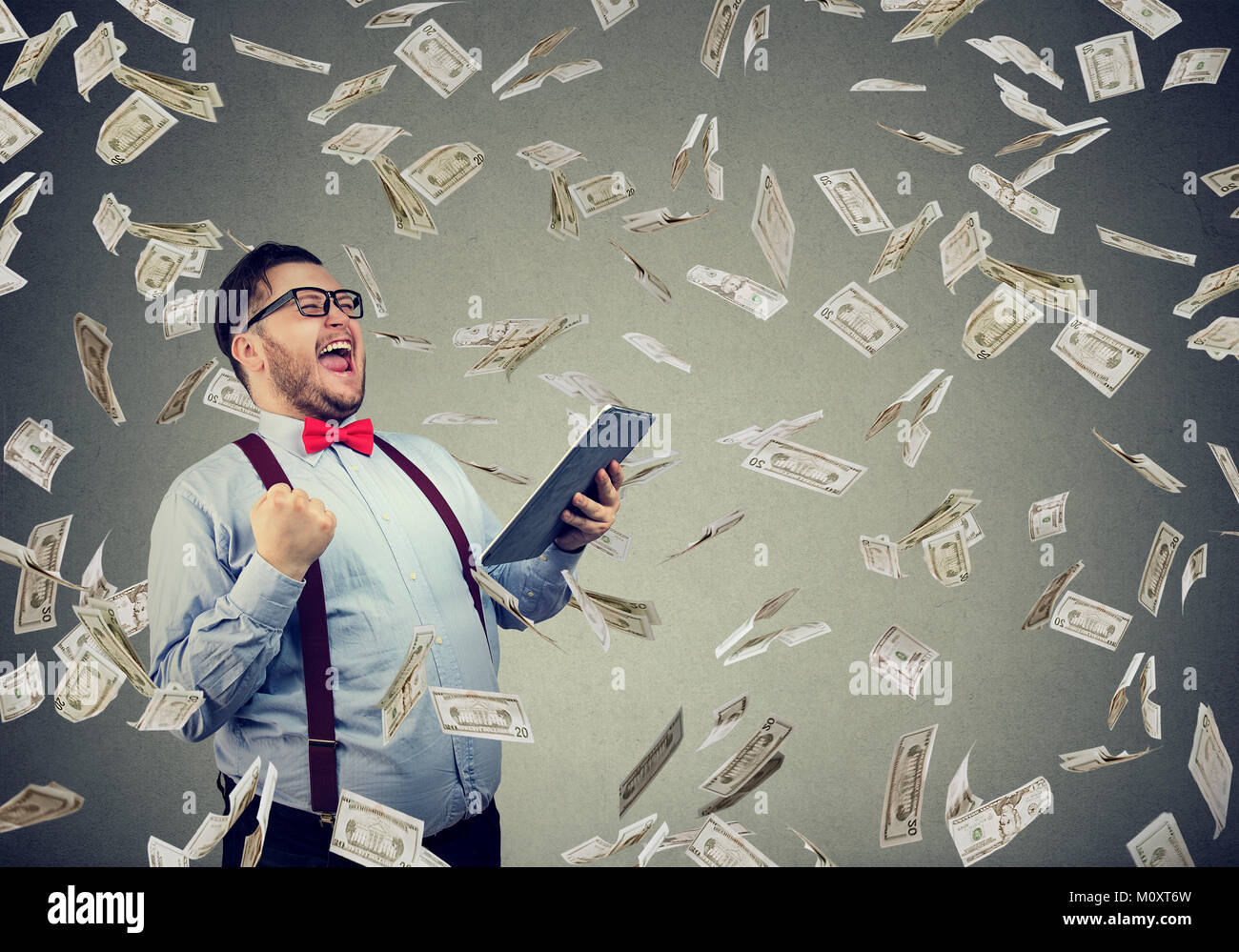 Happy man using tablet et posant avec triomphe en battant des dollars. Banque D'Images
