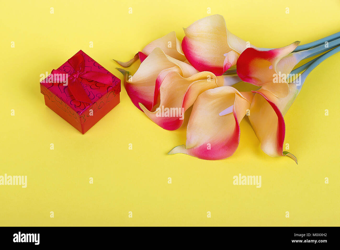 Bouquet de lis calla jaune rouge avec boîte cadeau rouge et ruban sur fond de carton jaune Banque D'Images