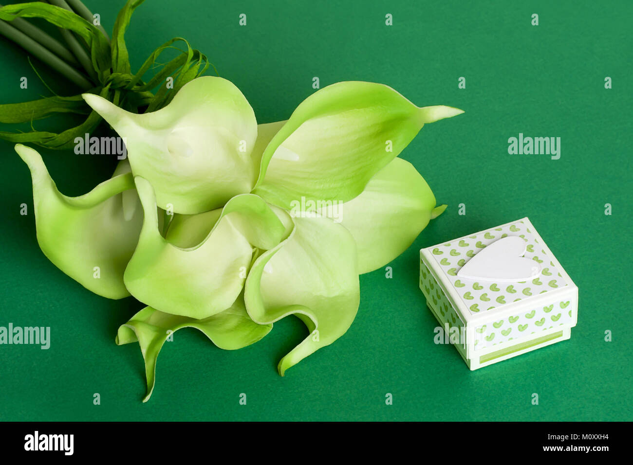 Bouquet de lis calla jaune vert avec boîte cadeau et coeur blanc sur fond de carton vert Banque D'Images