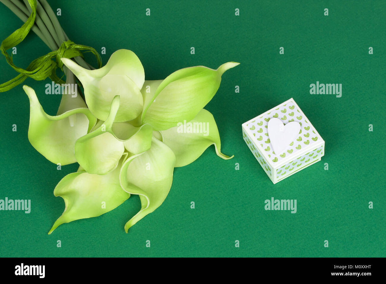 Bouquet de lis calla jaune vert avec boîte cadeau et coeur blanc sur fond de carton vert Banque D'Images